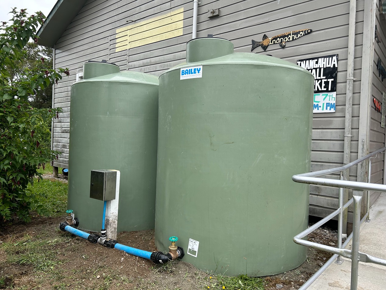 Two cylindrical green water tanks outside a wooden building