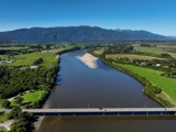 Aerial view of a road bridge crossing a broad river, looking upriver towards mountains