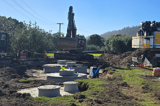An underground septic wastewater system under construction, with an excavator in the background and the tops of buried storage tanks and a pump chamber in the foreground.