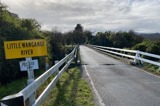 A view of the approach to a small two-lane road bridge over a river, yellow sign 'Little Wanganui River' in foreground