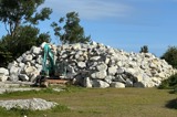 An excavator parked in front of a large stockpile of rocks to be used for flood protection rockwall construction