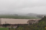 View of a river in flood from a terrace on an overcast day with farmland in the background 