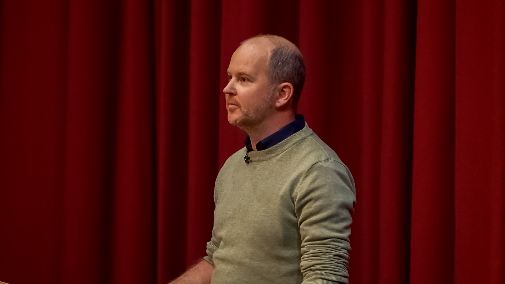 Man standing in front of red curtain giving a speech