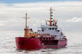 A red hopper suction dredge working at the mouth of a river with clouds and the open sea in the background